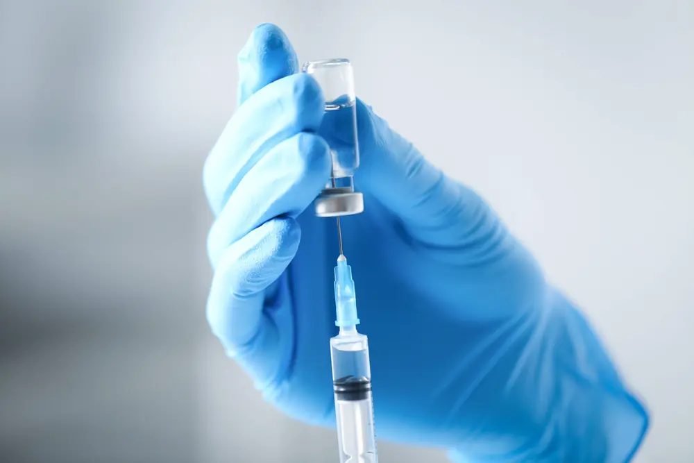 Gloved hand drawing a dose from a pharmaceutical vial